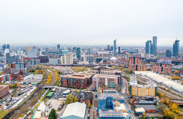 Aerial view of Manchester cityscape with modern skyscrapers, mid-rise buildings, rail tracks, and ongoing construction.