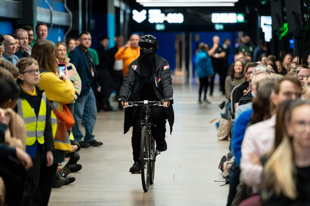 woman cycling through audience wearing veil and cycling helmet